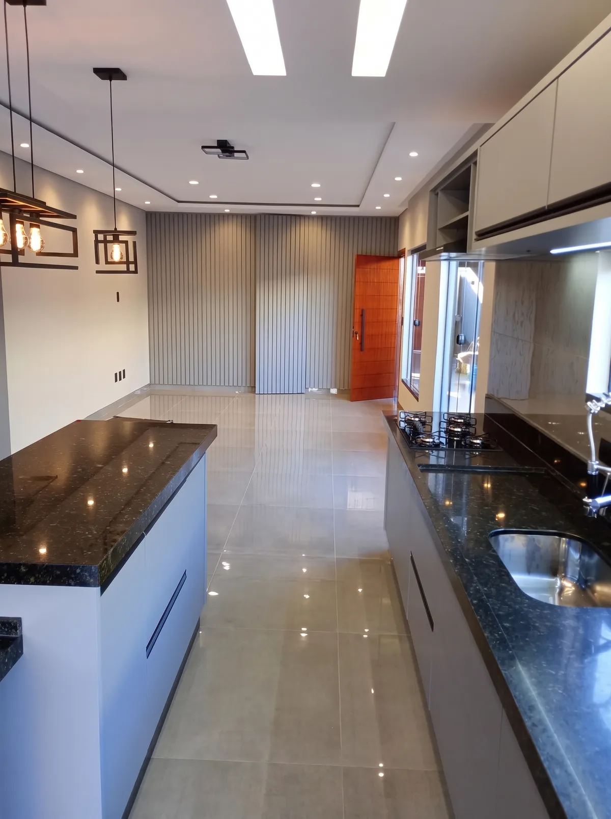 Cozinha planejada com ilha e bancada longa de granito preto, armários claros e painel ripado ao fundo