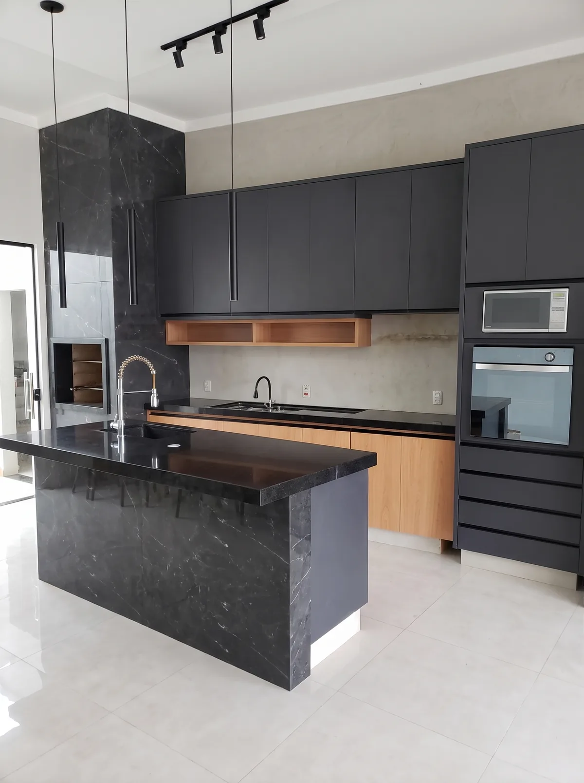 Cozinha planejada preta com base amadeirada, torre de fornos e ilha de granito